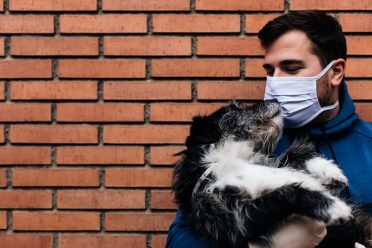 A man not letting his dog kiss him directly by wearing a mask to be safe during the Coronavirus pandemic